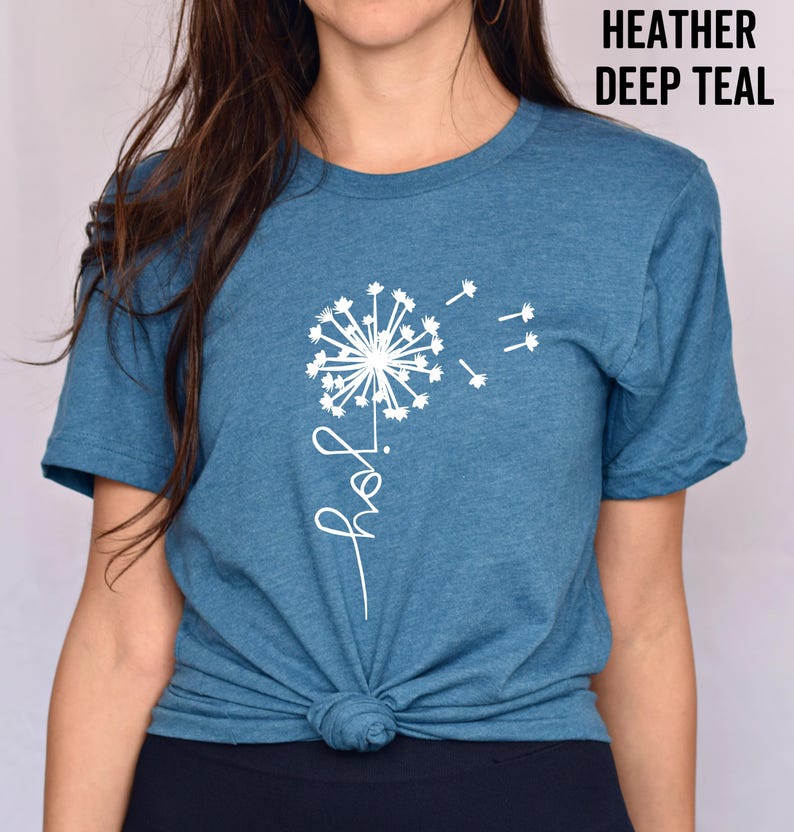 K&ouml;nnte beinhalten: Ein T-Shirt in der Farbe Heide-Tiefblau mit einem wei&szlig;en L&ouml;wenzahnmuster und dem Wort "Freude" in kursiv.