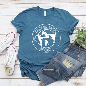 May include: A teal blue t-shirt with a white graphic that says "Easily Distracted by Goats" with a circle around the text and three goats inside the circle.