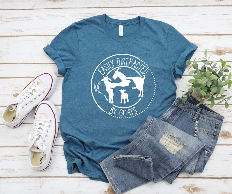 May include: A teal blue t-shirt with a white graphic that says "Easily Distracted by Goats" with a circle around the text and three goats inside the circle.