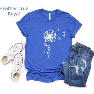 K&ouml;nnte beinhalten: Ein k&ouml;nigsblaues T-Shirt mit einem wei&szlig;en L&ouml;wenzahnmuster und dem Wort "Freude" in kursiv.