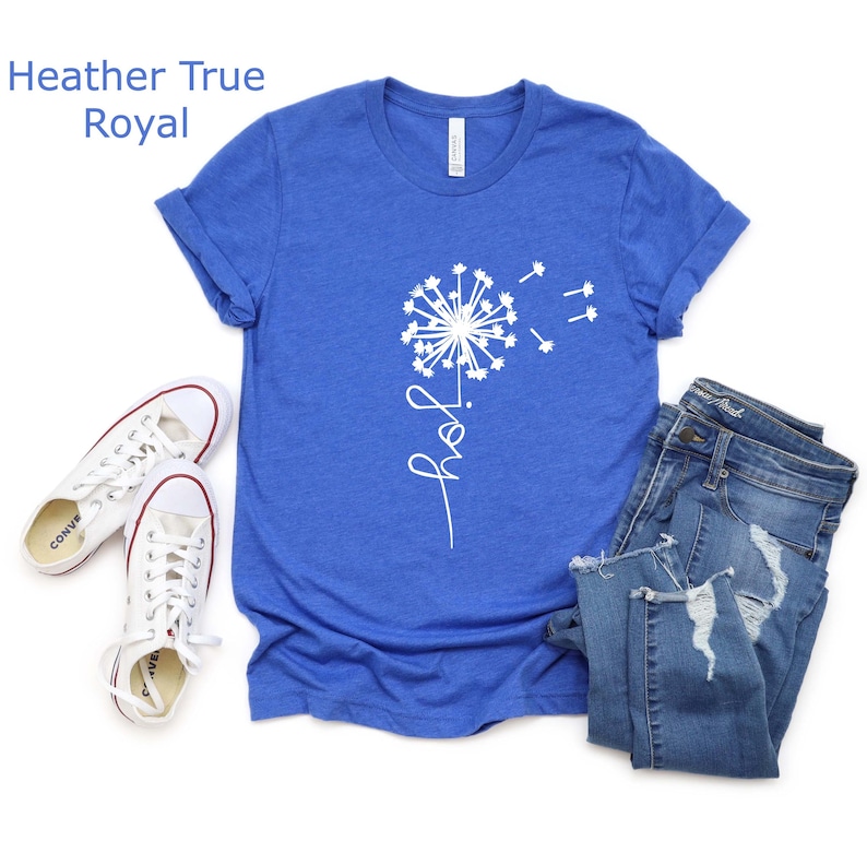 K&ouml;nnte beinhalten: Ein k&ouml;nigsblaues T-Shirt mit einem wei&szlig;en L&ouml;wenzahnmuster und dem Wort "Freude" in kursiv.