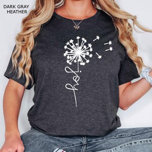 K&ouml;nnte beinhalten: Ein dunkelgraues T-Shirt mit einem wei&szlig;en L&ouml;wenzahnmuster und dem Wort "grow" in Kursivschrift.