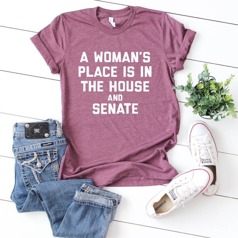 May include: A maroon t-shirt with the text "A woman's place is in the house and senate" printed in white.