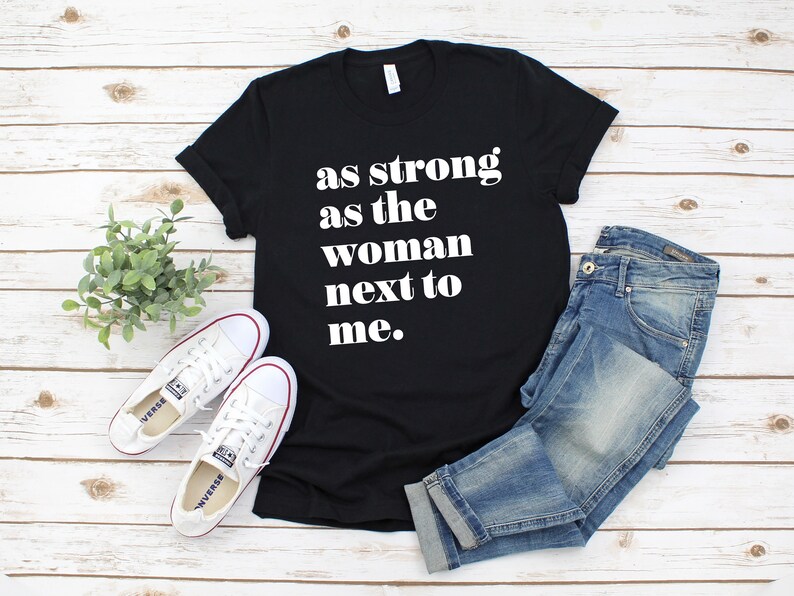 May include: Black t-shirt with white text that reads "as strong as the woman next to me."