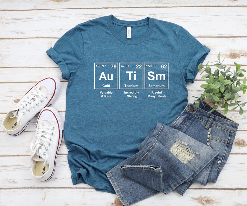 May include: A teal blue t-shirt with a white graphic of the periodic table elements for gold, titanium, and samarium. The graphic includes the element symbol, atomic number, atomic weight, and name. The text below each element reads "Valuable & Rare", "Incredibly Strong", and "Useful Many talents".