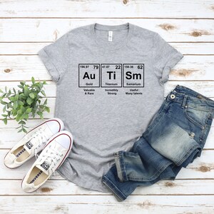 May include: A gray t-shirt with a graphic of the periodic table elements Au, Ti, and Sm. The graphic includes the atomic number, atomic weight, and element name for each element. The text below the graphic reads "Valuable & Rare", "Incredibly Strong", and "Useful Many talents".