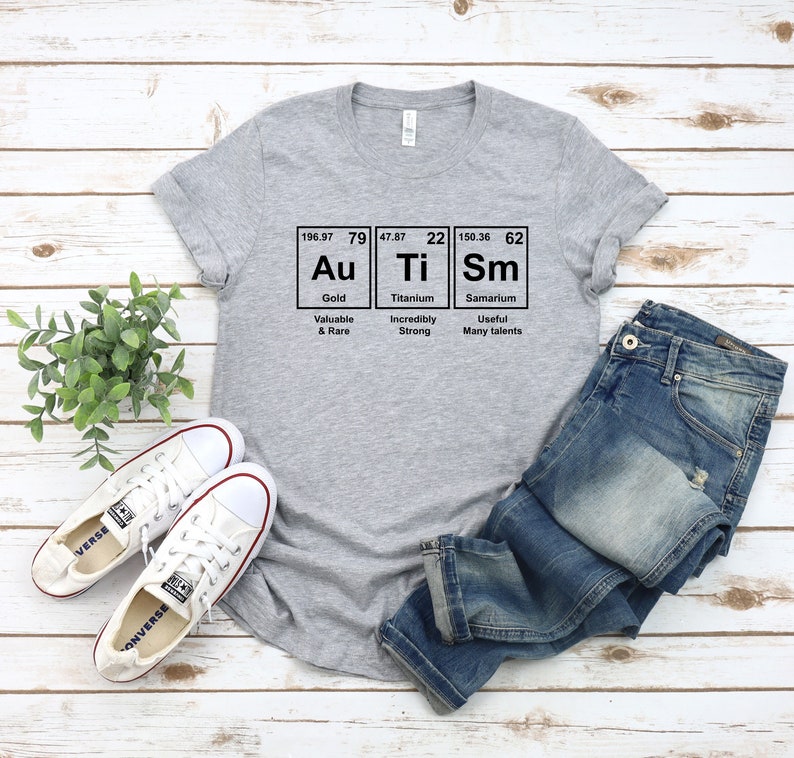 May include: A gray t-shirt with a graphic of the periodic table elements Au, Ti, and Sm. The graphic includes the atomic number, atomic weight, and element name for each element. The text below the graphic reads "Valuable & Rare", "Incredibly Strong", and "Useful Many talents".