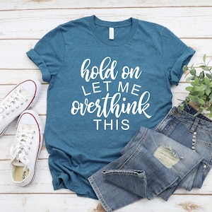 Pode incluir: Uma camiseta azul turquesa com o texto "hold on let me overthink this" em letras brancas.