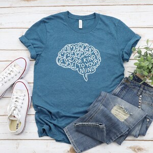May include: A teal blue t-shirt with a white outline of a brain with hearts inside and the text "Be Kind To Your Mind".