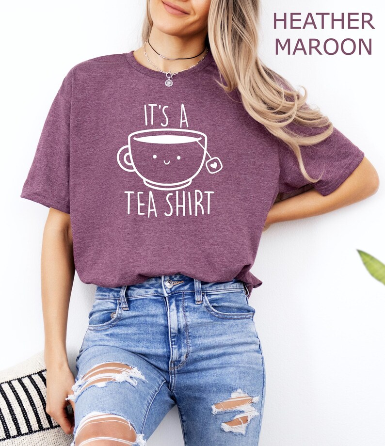 May include: A heather maroon t-shirt with a white graphic of a teacup with a smiling face and the text "It's a Tea Shirt".