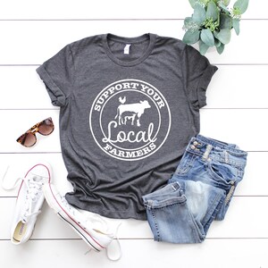 May include: A dark gray t-shirt with a white circle graphic that says "Support Your Local Farmers" with a cow, chicken, and calf inside the circle.