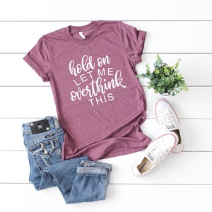 Pode incluir: Uma camiseta de cor vinho com o texto "hold on let me overthink this" em letras brancas.