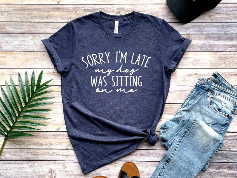 Op de afbeelding: Een donkerblauw T-shirt met witte tekst die "Sorry, ik ben te laat, mijn hond zat op me" zegt.