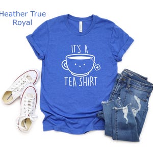 May include: A royal blue t-shirt with a white graphic of a teacup with a smiling face and the text "It's a Tea Shirt".