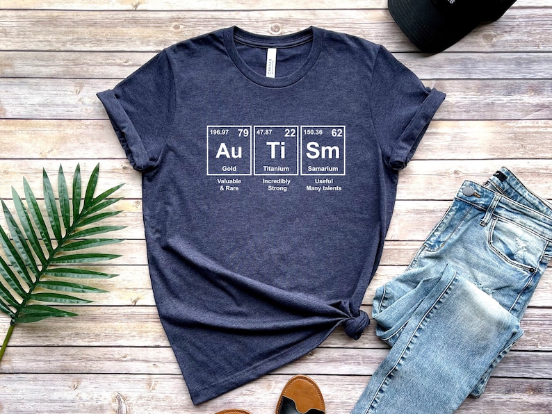May include: A navy blue t-shirt with a white graphic of the periodic table elements Au, Ti, and Sm. The graphic includes the atomic number, atomic weight, and name of each element. The text below each element describes its properties: Gold - Valuable & Rare, Titanium - Incredibly Strong, Samarium - Useful Many talents.