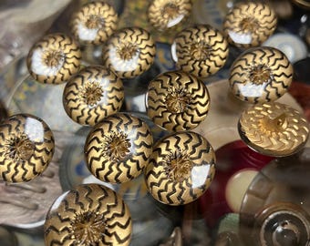 May include: A collection of 12 gold and black buttons with a zig-zag pattern. The buttons are round and have a raised center.
