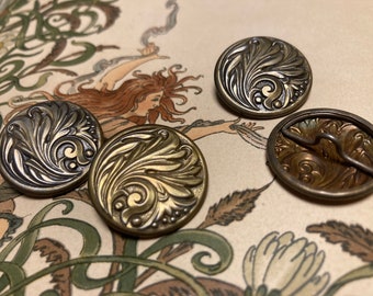 May include: Four antique brass buttons with a decorative floral design. The buttons have a raised, textured surface and a circular shape.