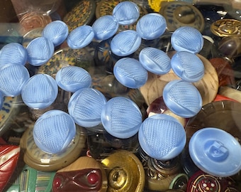May include: A collection of light blue buttons with a textured design. The buttons are arranged in a random pattern on a surface with other buttons and objects.