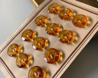 May include: A card with twelve amber glass buttons with a star-shaped design. The buttons are arranged in rows on a brown card with a brown border.