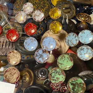 Può includere: Una collezione di vari bottoni decorativi in diversi colori e design. I bottoni includono rosso, giallo, blu e verde con accenti dorati e marroni. Alcuni bottoni hanno un aspetto marmorizzato.