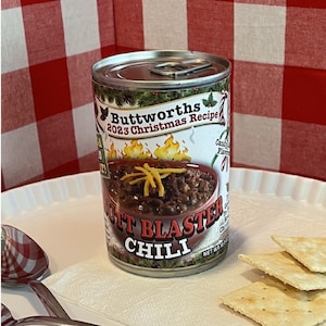 Puede incluir: Una lata roja y blanca de Buttworths Butt Blaster Chili, receta de Navidad 2023. La lata tiene una imagen de chili con queso y una caña de caramelo roja y blanca.