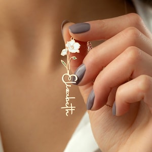 This is a personalization necklace with colored Poppy August birth month flower. Its leaves are green, its flower is white. The necklace stands vertical on the model’s hand.