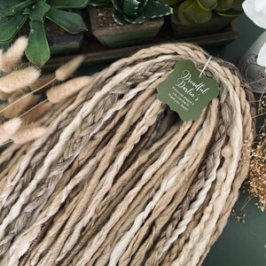 Puede incluir: Un paquete de rastas sintéticas marrones y blancas con una etiqueta que dice "Dreadful Darlin's If you can dream it, you can be it! Thank you, Darlin'"