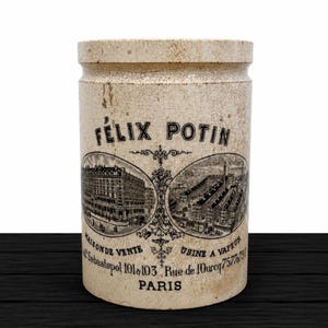 May include: A cylindrical ceramic crock with a cream-colored crackle glaze finish. The front features black printed text reading FELIX POTIN, PARIS, and two oval illustrations of buildings, with additional French text detailing the business address.