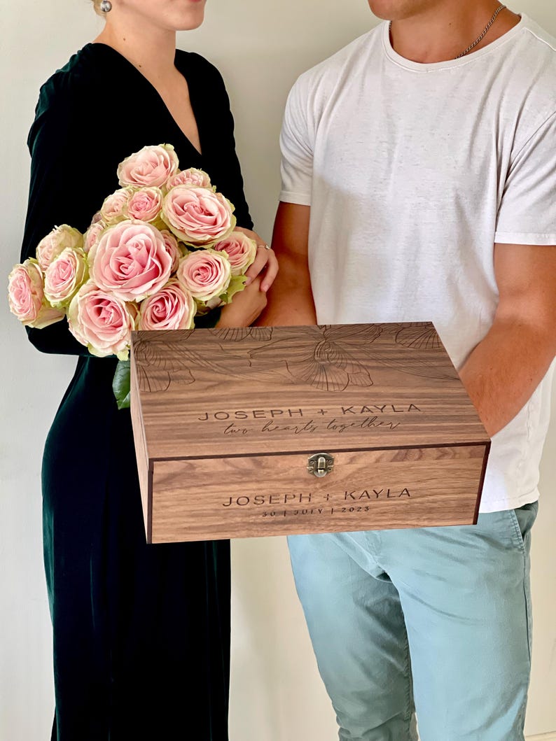 May include: A wooden keepsake box with floral engravings and the names "Joseph + Kayla" and the phrase "two hearts together" engraved on the lid. The box also includes the date "30 JULY | 2023".