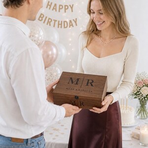 May include: A wooden box with the initials "M/R" and the names "Mark & Rebecca" engraved on the lid. The box is being presented as a gift. A "Happy Birthday" banner is in the background.
