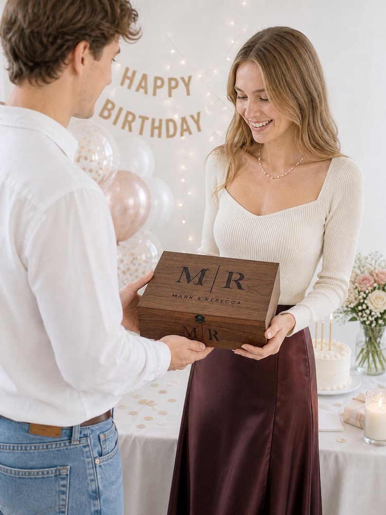 May include: A wooden box with the initials "M/R" and the names "Mark & Rebecca" engraved on the lid. The box is being presented as a gift. A "Happy Birthday" banner is in the background.