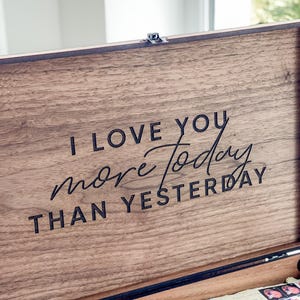 May include: Wooden keepsake box with the text "I LOVE YOU more today THAN YESTERDAY" engraved on the lid. The box is open, revealing cards and other items inside. The wood has a natural grain.