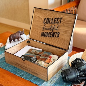 Può includere: Una scatola rettangolare in legno per ricordi con coperchio incernierato. L'interno del coperchio presenta il testo nero "COLLECT beautiful MOMENTS". Il pannello esterno anteriore mostra il testo "OPEN TO DIVE INTO THE SEA OF PLEASANT MEMORIES". La scatola contiene vari fogli e fotografie.
