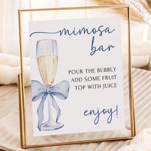 May include: A framed sign with the words "mimosa bar" in navy blue script. The sign features a watercolor illustration of a champagne flute with a blue bow. Text below reads "Pour the bubbly, add some fruit, top with juice, enjoy!"