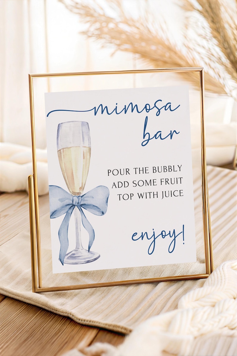 May include: A framed sign with the words "mimosa bar" in navy blue script. The sign features a watercolor illustration of a champagne flute with a blue bow. Text below reads "Pour the bubbly, add some fruit, top with juice, enjoy!"
