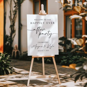 Peut inclure: Un panneau blanc sur un chevalet en bois avec les mots "WELCOME TO OUR HAPPILY EVER AFTER PARTY" en &eacute;criture noire. Le panneau c&eacute;l&egrave;bre Megan & Kyle le 7 ao&ucirc;t 2025. L'arri&egrave;re-plan comprend de la verdure et un b&acirc;timent.
