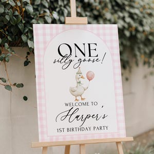 Puede incluir: Un caballete de madera exhibe un letrero a cuadros rosas y blancos. El letrero dice "ONE silly goose!" encima de un ganso de dibujos animados con un globo. Debajo, dice "WELCOME TO Harper's 1st BIRTHDAY PARTY".
