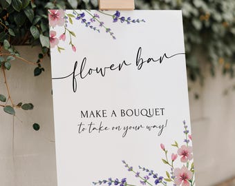 May include: A white sign on a wooden easel with the words "flower bar" in cursive script. The sign also reads "MAKE A BOUQUET to take on your way!" Floral watercolor designs in pink and purple decorate the corners.
