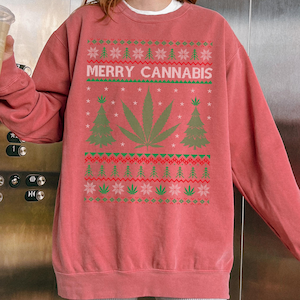 May include: A red-orange sweatshirt with a green and red holiday-themed design. The design includes a large cannabis leaf, Christmas trees, and the text "MERRY CANNABIS" in white.