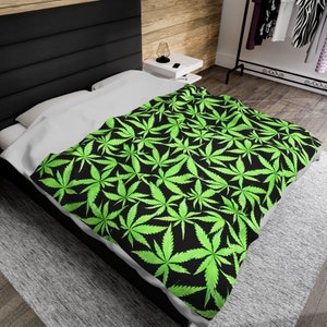 May include: A black and green bedding set with a marijuana leaf pattern. The bedding is on a bed with a white pillow and a black headboard.