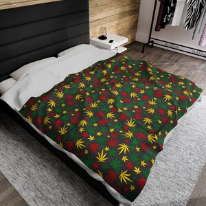 May include: A black bed with a white duvet cover and a green, red, and yellow patterned throw blanket featuring a repeating leaf design.