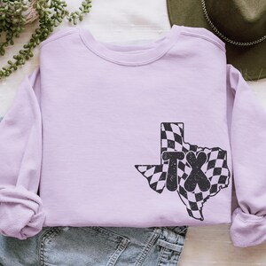 May include: A lavender sweatshirt with a black and white checkered outline of the state of Texas with the letters "TX" inside.