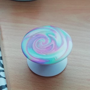 Pode incluir: Um suporte de telefone branco com um padr&atilde;o de redemoinho de rosa, azul e verde.