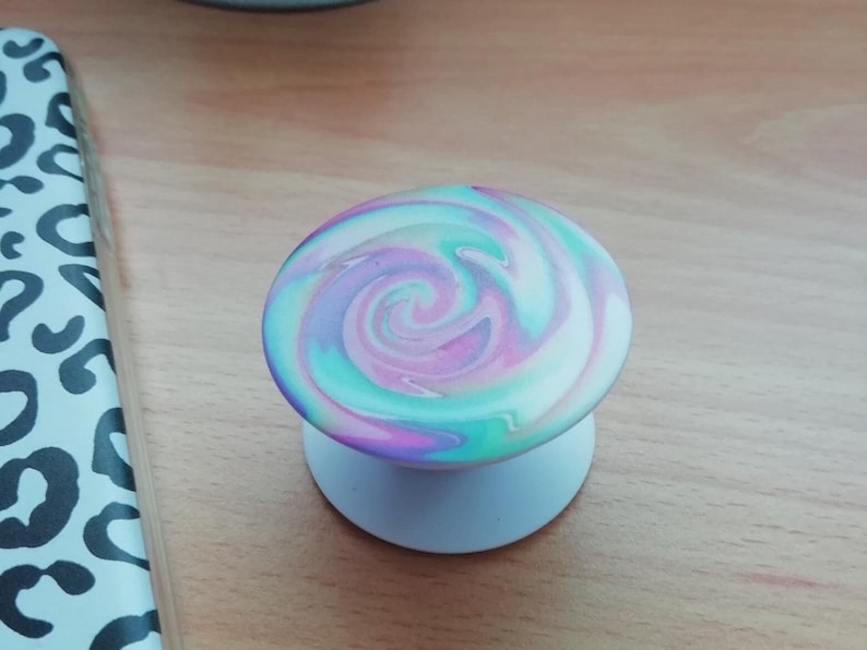 Pode incluir: Um suporte de telefone branco com um padr&atilde;o de redemoinho de rosa, azul e verde.