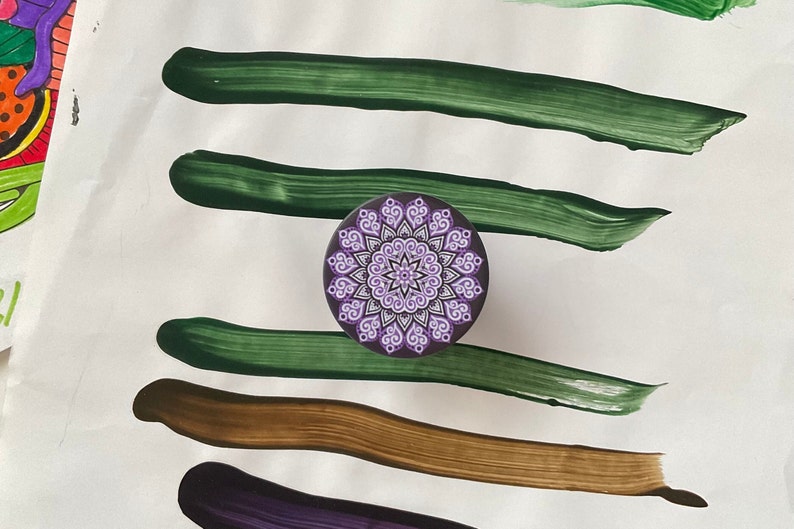 Pode incluir: Um design de mandala roxo e branco sobre um fundo preto. O mandala &eacute; cercado por quatro pinceladas verdes sobre um fundo branco.