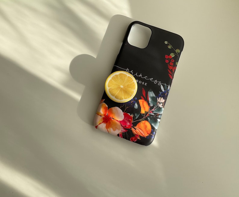 Pode incluir: Capa de telefone preta com um design floral com flores vermelhas, laranja, amarelas e azuis. O texto "princess rose" est&aacute; impresso na capa. Uma fatia de lim&atilde;o est&aacute; em cima da capa.
