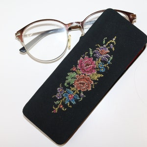 May include: A black eyeglass case with a floral embroidery design. The embroidery features colorful flowers in shades of pink, red, yellow, blue, and green.
