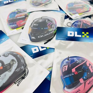 Puede incluir: Surtido de ambientadores para coche con diversos cascos de pilotos de F&oacute;rmula 1. Los ambientadores est&aacute;n envasados en bolsas de pl&aacute;stico transparentes con un logotipo DLX negro y amarillo. Los cascos est&aacute;n impresos con varios patrocinadores y logotipos, incluidos Williams Racing, Myprotein y Duracell.
