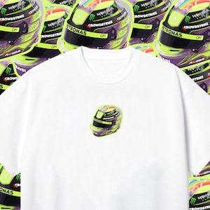 Könnte beinhalten: Weißes T-Shirt mit einem Aufdruck eines lila und grünen Rennhelms mit einem Regenbogen-Design auf der Oberseite. Der Helm trägt die Aufschrift "Petronas" und "Crowdstrike".