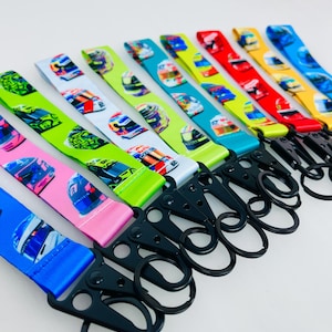 K&ouml;nnte beinhalten: Ein Set aus zehn bunten Lanyards mit einem Rennhelm-Muster und schwarzen Metall-Schl&uuml;sselanh&auml;ngern. Die Lanyards sind in verschiedenen Farben, darunter Gr&uuml;n, Blau, Rot, Gelb und Pink.